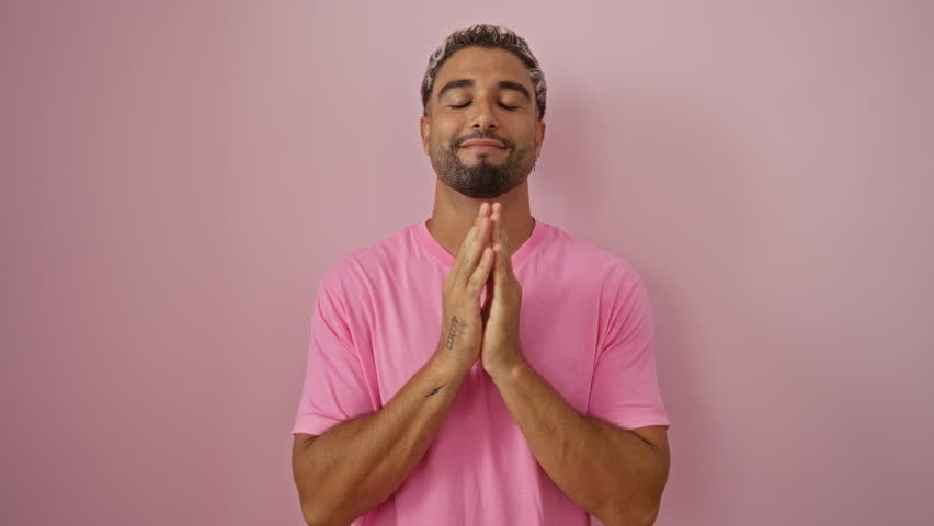 Young arab man smiling and holding hands together over isolated pink background