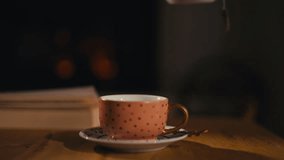 Close-up of a female hand pouring hot tea from a teapot into a cup, creating a cozy ambiance with a warm fireplace in the background. Concept of relaxation and warmth. Slow motion - Powered by Shutterstock - Get 15% off with code: PIKWIZARD15