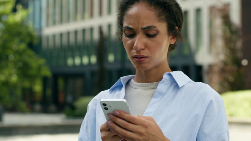 African American business woman in city urban outside office girl female businesswoman entrepreneur looking mobile phone reading bad news upset sad frustrated problem online holding smartphone chat