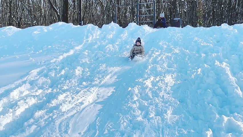 Sledding in winter park, snow weather. Child slides down. Children ski in the winter with a slide on the tubing. kid runs to hill and sledding down by the tube. winter leisure