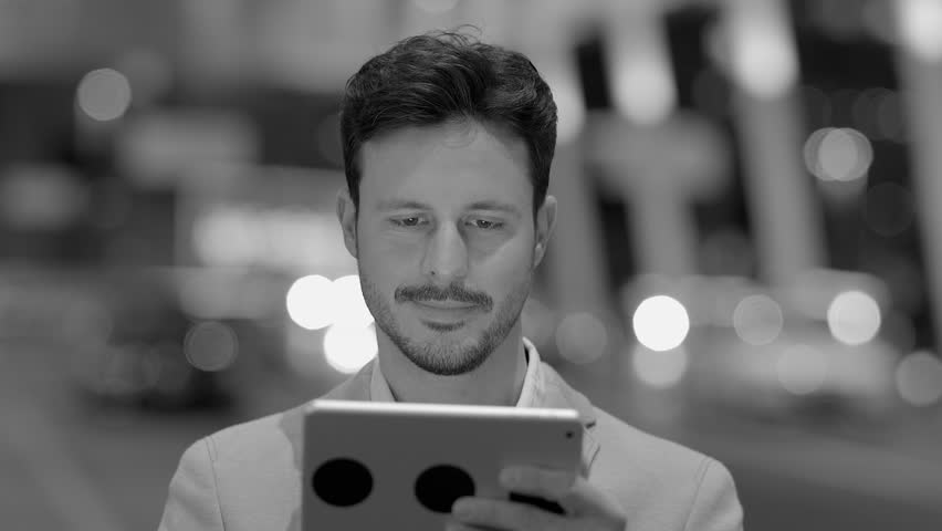 Black and White of a Man Using Tablet against the Backdrop of a Bustling Street