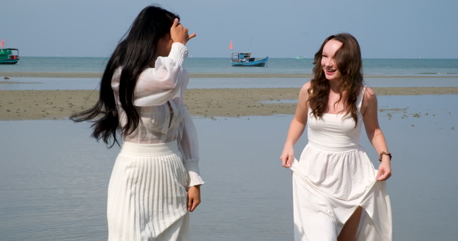 two girls friends walking on the beach LGBT white dress run dancing beautiful young women asian european female against the background of the sea river shallow water