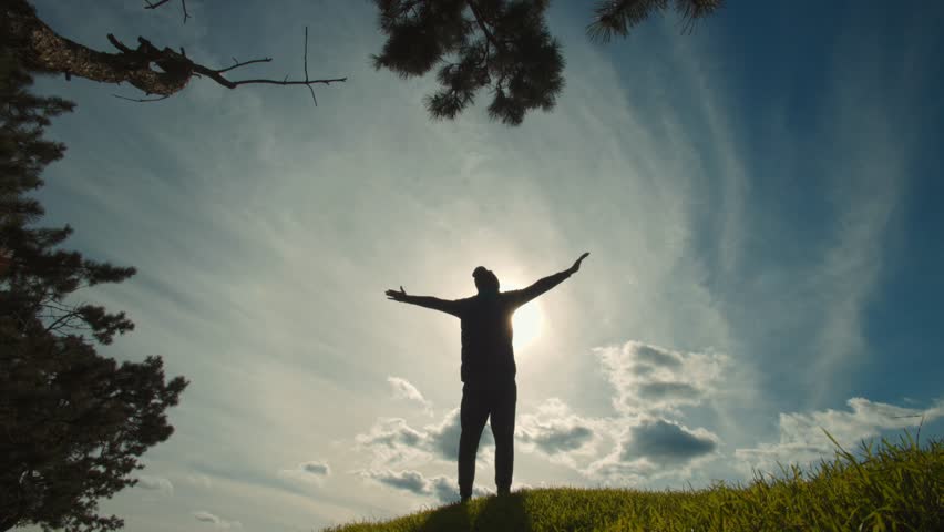 As the sun illuminates the horizon, a man stands with arms outstretched, embracing a victorious and liberating moment under the open sky in this peaceful landscape.
