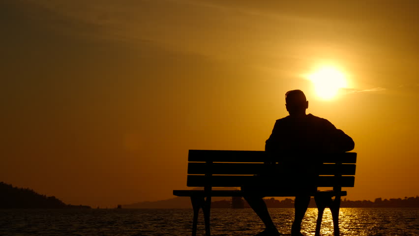 Man look at beautiful nightfall. A cute silhouette of resting man on bench. A tourist enjoy the river view during nightfall time.