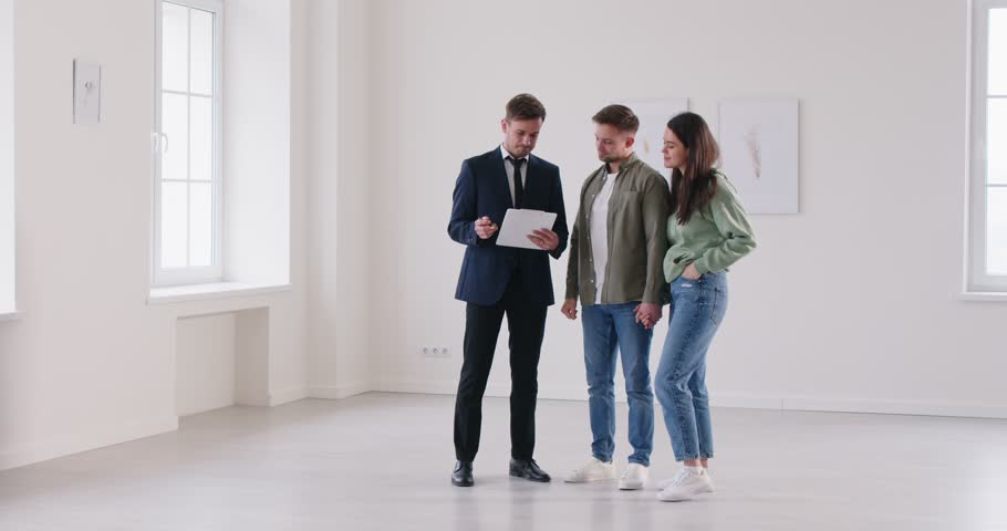 Young happy smiling couple reaching agreement with realtor and going to sign a deal with a real estate agent. Successful family ready to become homeowners. Real estate market concept. 4k video.