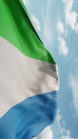 Wavy flag of Sierra Leone blowing in the wind in slow motion. Waving official Sierra Leone flag team symbol abstract vertical background. Blue sky with clouds. World countries flying flags concept