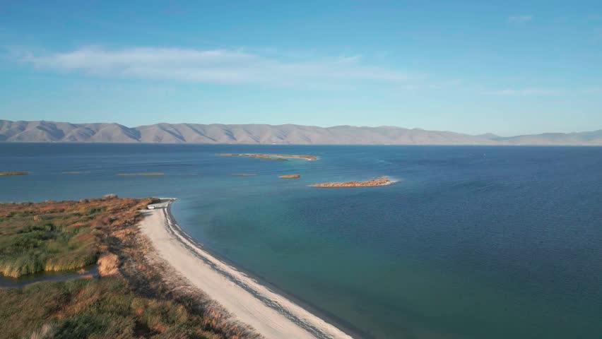 Drone footage mountain lake. Aerial view on Sevan lake in Armenia, West Asia. Aerial shot Beach with grass, blue lake with mountains  background. Tourism in  Caucasus. Wild adventure. Discovery Asia.
