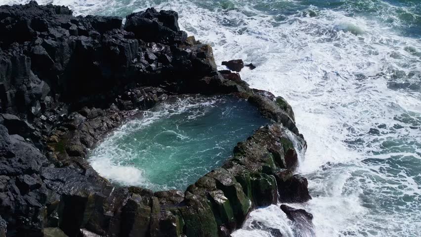 Aerial view of a natural pool surrounded by rugged rocks and crashing waves, Brimketill, Iceland.