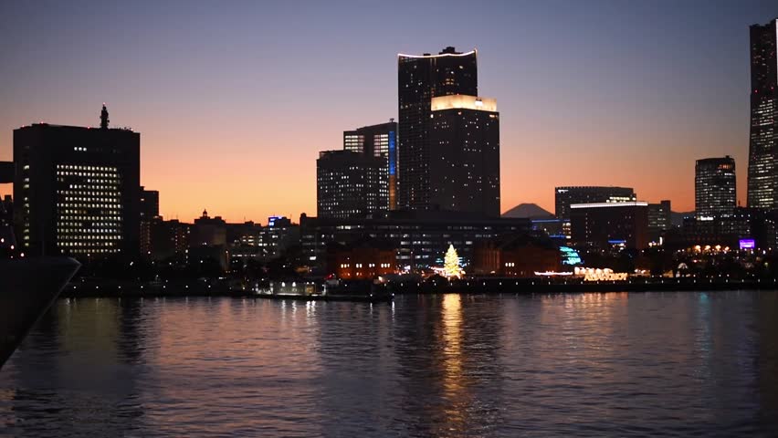 Beautiful orange sunset above the skyline and waterfront of Yokohama minato mirai. Mount fuji visible between skyscrapers with a big wheel. Soft reflection in the water almost night