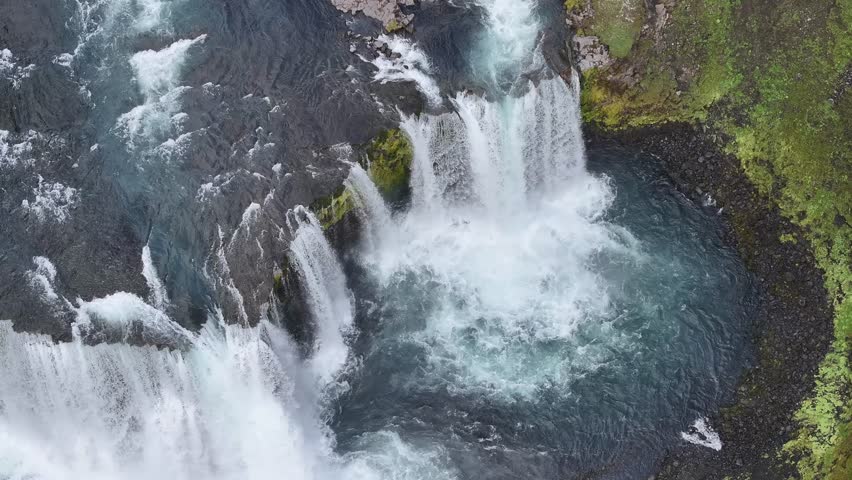 Aerial view of a breathtaking waterfall cascading into a serene river surrounded by vibrant greenery, Axalfoss, Iceland.