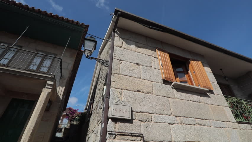 A traditional stone house with wooden shutters under a bright blue sky in Pontevedra, Spain