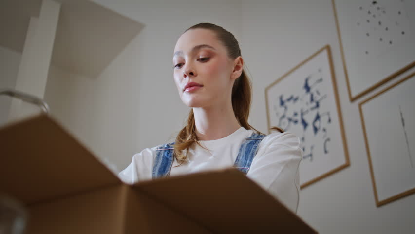 Smiling lady unpacking household items in new home feeling happy closeup. Cheerful woman taking wrapped vase with bubble wrap from cardboard box at own real estate. Girl enjoy moving into modern flat.