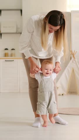 mom teaches the baby to walk at home, the baby boy learns to walk by taking the first steps holding his mother's hand