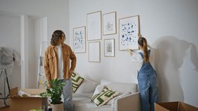 Family couple decorating home by hanging artwork together. Happy woman man collaborating to arrange paintings on modern living room wall. Young spouses creating stylish contemporary apartment space. - Powered by Shutterstock - Get 15% off with code: PIKWIZARD15
