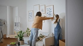 Married couple hanging artwork on wall new home. Happy woman and man working together carefully placing paintings in living room. Romantic spouses decorating new apartment creating stylish atmosphere. - Powered by Shutterstock - Get 15% off with code: PIKWIZARD15