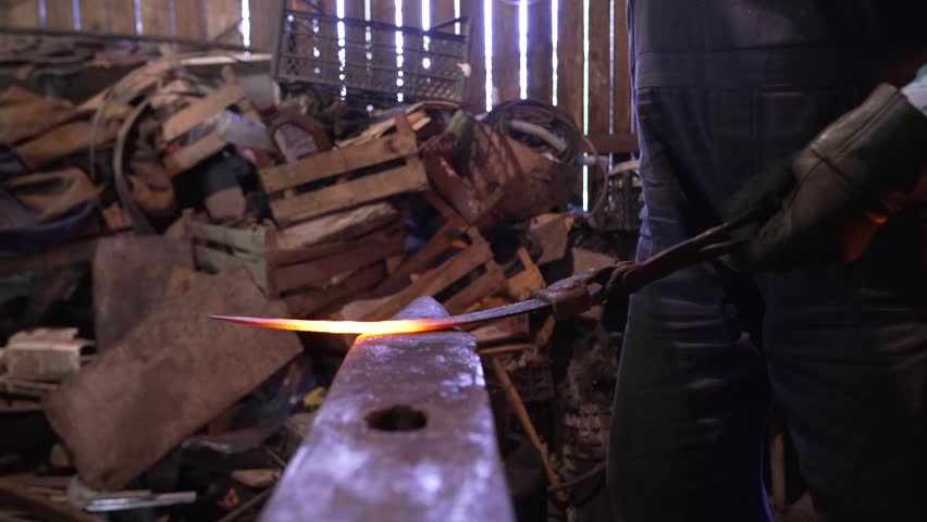 An old man shapes knife from heated iron in his work shop