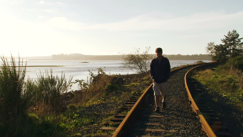 Model released man walks toward camera along railroad tracks near waterway in