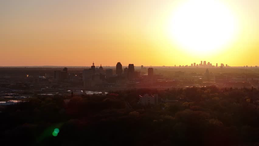 A drone showing the skyline of Minneapolis city and St Paul at sunset with Mississippi river in Minnesota, against yellow orange sky