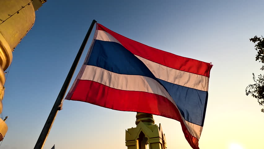 Thai flag waving proudly at sunset near a historic temple in Thailand, highlighting beautiful colors and cultural significance
