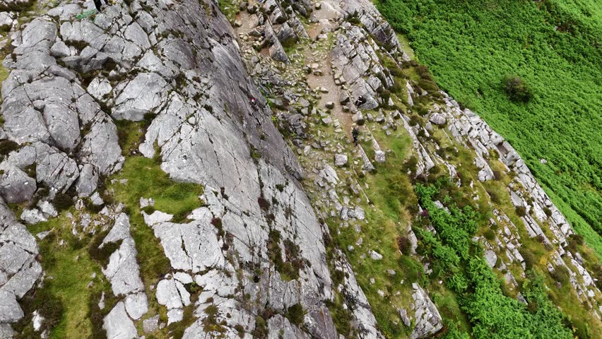 A young climber ascending the dramatic Barmouth slabs in North Wales, with stunning views of hills and coastlines below.