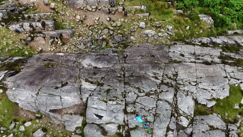 A young climber ascending the dramatic Barmouth slabs in North Wales, with stunning views of hills and coastlines below.