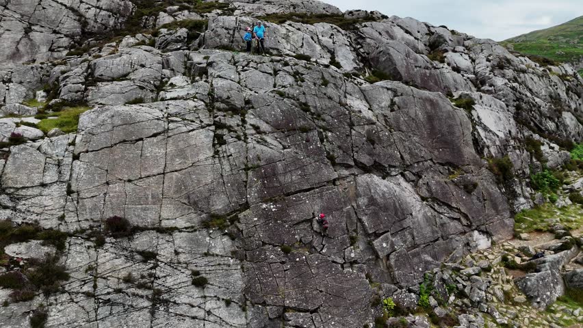 A young climber ascending the dramatic Barmouth slabs in North Wales, with stunning views of hills and coastlines below.