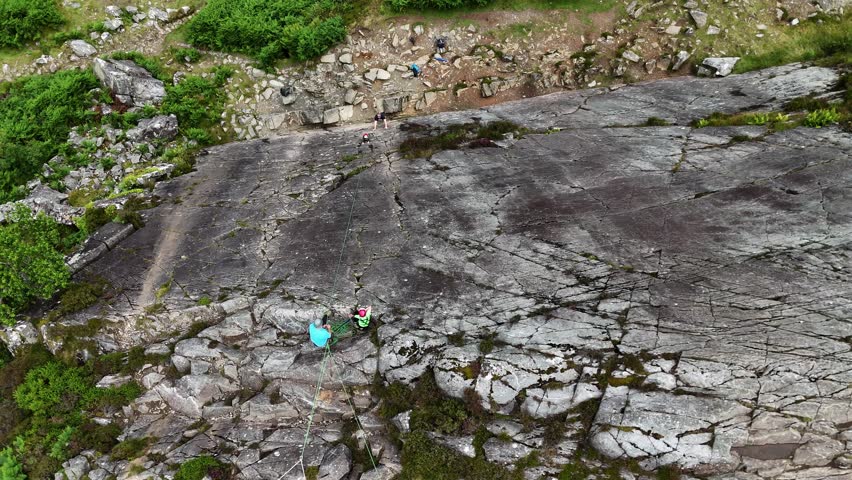A young climber ascending the dramatic Barmouth slabs in North Wales, with stunning views of hills and coastlines below.