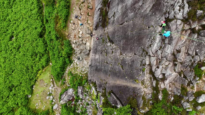 A young climber ascending the dramatic Barmouth slabs in North Wales, with stunning views of hills and coastlines below.