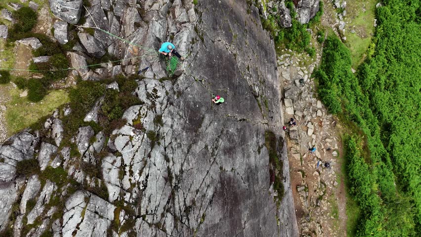 A young climber ascending the dramatic Barmouth slabs in North Wales, with stunning views of hills and coastlines below.