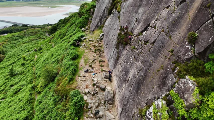 A young climber ascending the dramatic Barmouth slabs in North Wales, with stunning views of hills and coastlines below.