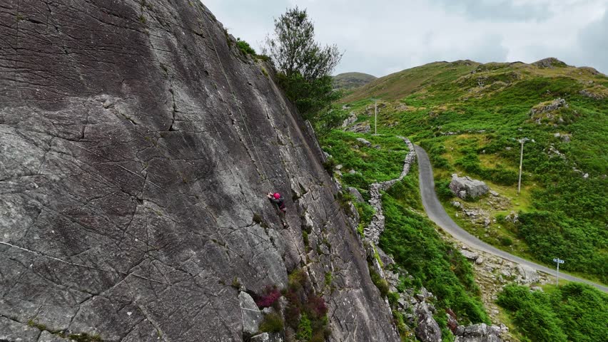 A young climber ascending the dramatic Barmouth slabs in North Wales, with stunning views of hills and coastlines below.