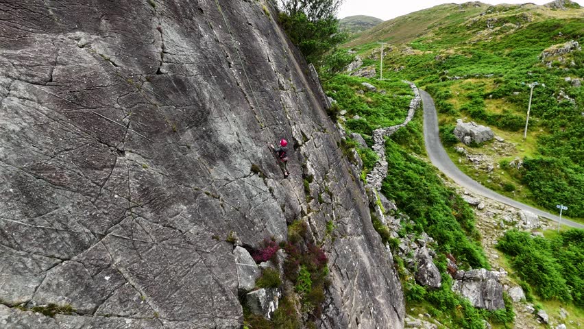 A young climber ascending the dramatic Barmouth slabs in North Wales, with stunning views of hills and coastlines below.