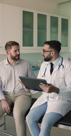 Attentive Hispanic man professional doctor in white coat holds clipboard listening to patient health complaints, take notes in medical card, analyze information. Regular check-up in clinic. Medicine