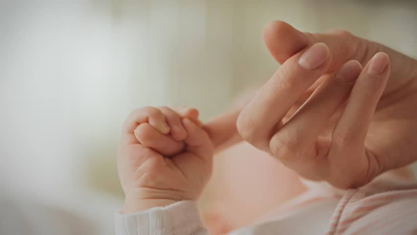 A small baby hand gently holds onto a parent's finger, displaying a deep bond and affection in a soft, serene environment, emphasizing nurturing and connection in early moments of life