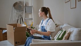 Young woman unpacking boxes in new home feeling thoughtful. Serious apartment owner sitting on couch living room taking books from cardboard package. Lady moving and feeling relaxed in house interior. - Powered by Shutterstock - Get 15% off with code: PIKWIZARD15