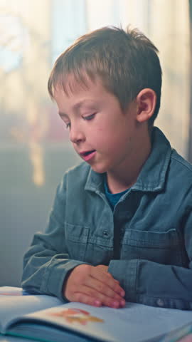 Vertical video close-up of a boy child reading a book in the nursery. Education and development of the child. High quality 4k footage