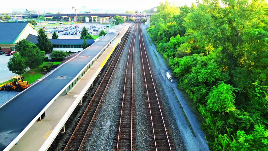 Gliding steadily over a set of railroad tracks, the view remains fixed in one direction. As the surrounding brush and trees on either side give way to new scenery, the station platform gradually comes