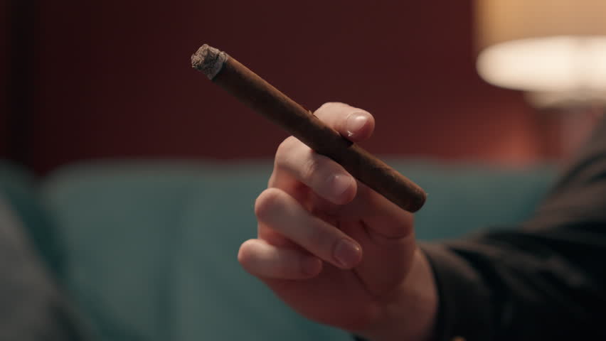 Close up unknown successful Caucasian man guy unrecognizable rich businessman male hand holding cigar smoking tipped cigarette ash home living room. Unhealthy lifestyle bad habit depression addiction