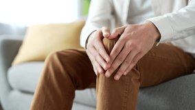 Male hands massaging knee leg muscles while sitting on sofa in living room at home. Young adult man suffers from painful severe knee joint pain, could not walk, illness, cramps, rheumatism. Close up - Powered by Shutterstock - Get 15% off with code: PIKWIZARD15