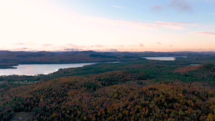 Timelapse of a serene sunrise over Schroon Lake, New York, showcasing colorful autumn forests, rolling mountains, and calm waters, with the sky gradually lighting up in soft morning hues.