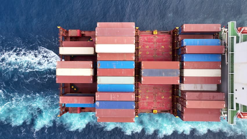 Aerial drone tracking video of truck size container cargo vessel cruising in deep blue sea near commercial port of Piraeus