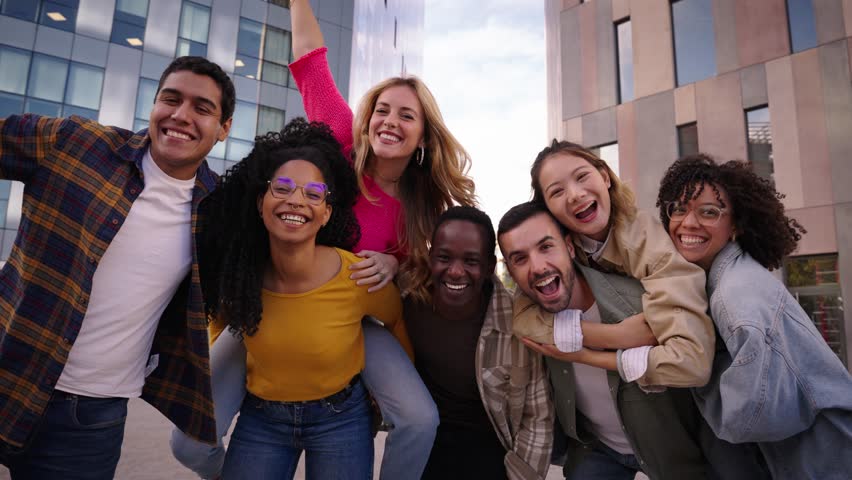 Group of diverse generation z piggyback joyful people having fun together posing excited in city. Happy young multiracial friends looking cheerful at camera standing in urban community outdoors