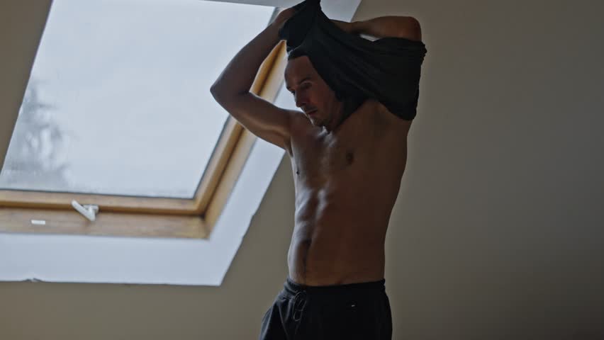 A Young Man is Changing His Clothes in a Brightly Lit Room Filled with Ample Natural Light. Slow motion