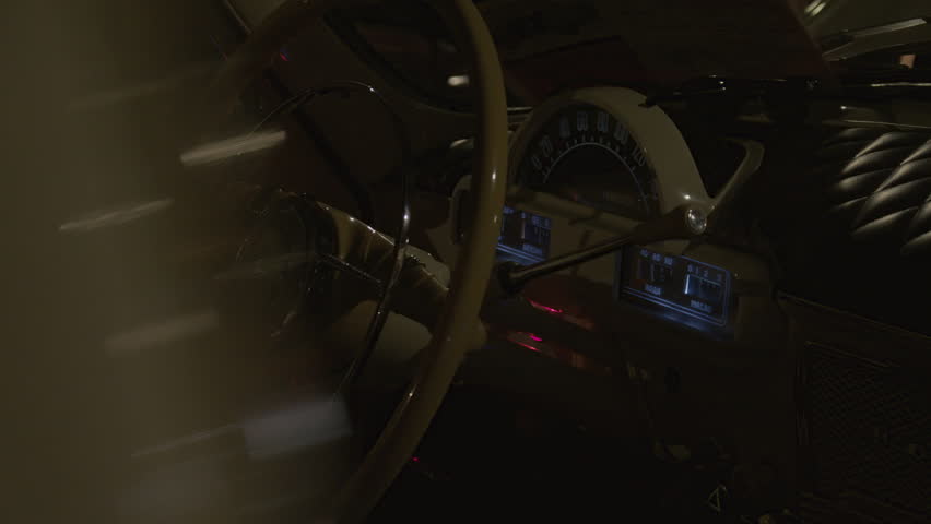 Close-up of a vintage car dashboard with a classic steering wheel and analog gauges, dimly lit interior. Inside a retro car cabin, illuminated with dim light.