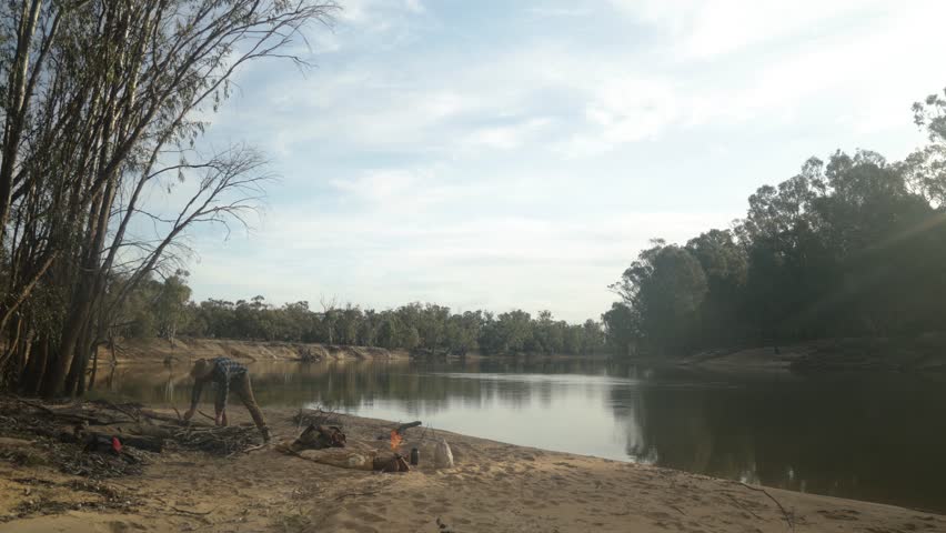 Traditional swagman makes a campfire on the banks of the Murray river in Australia.