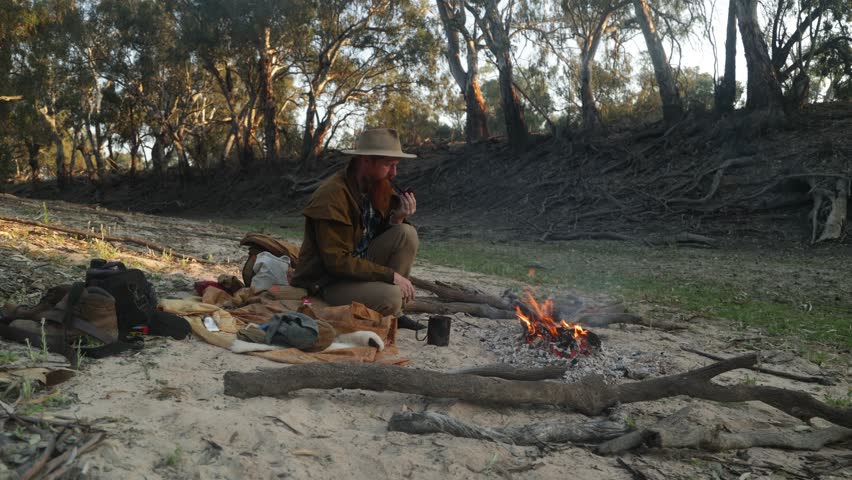 Traditional bushman sitting around a campfire in a river bed in the Australian outback.
