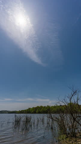 A vertical timelapse video of a total solar eclipse recorded from start to finish, with the darkened sun in a clear daytime sky above a calm lake.