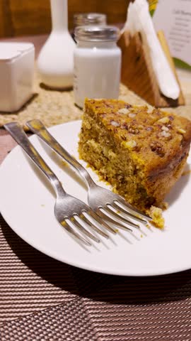 4K vertical shot of piece of Carrot cake on plate with forks. Cafe background.  Delicious dessert. Carrot cake slice eating. Sweet dessert.