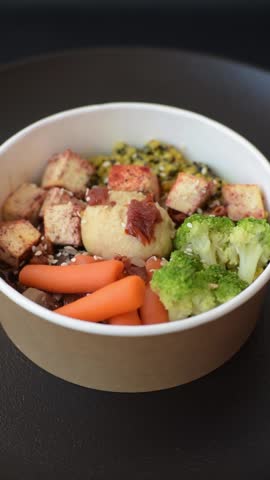 Colorful vegan vegetarian dish consists of tofu, broccoli, quinoa, mushrooms and carrots on a dark textured background