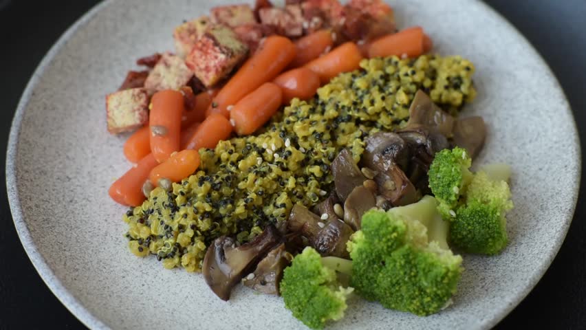 Colorful vegan vegetarian dish consists of tofu, broccoli, quinoa, mushrooms and carrots on a dark textured background